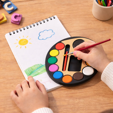 Child coloring with a paint palette and drawing book on a wooden table