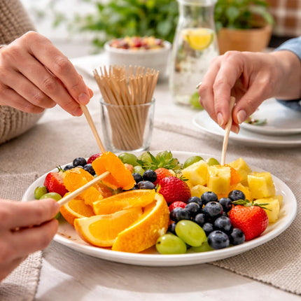 Fruit skewers being prepared on a plate with oranges, strawberries, grapes, and pineapple.